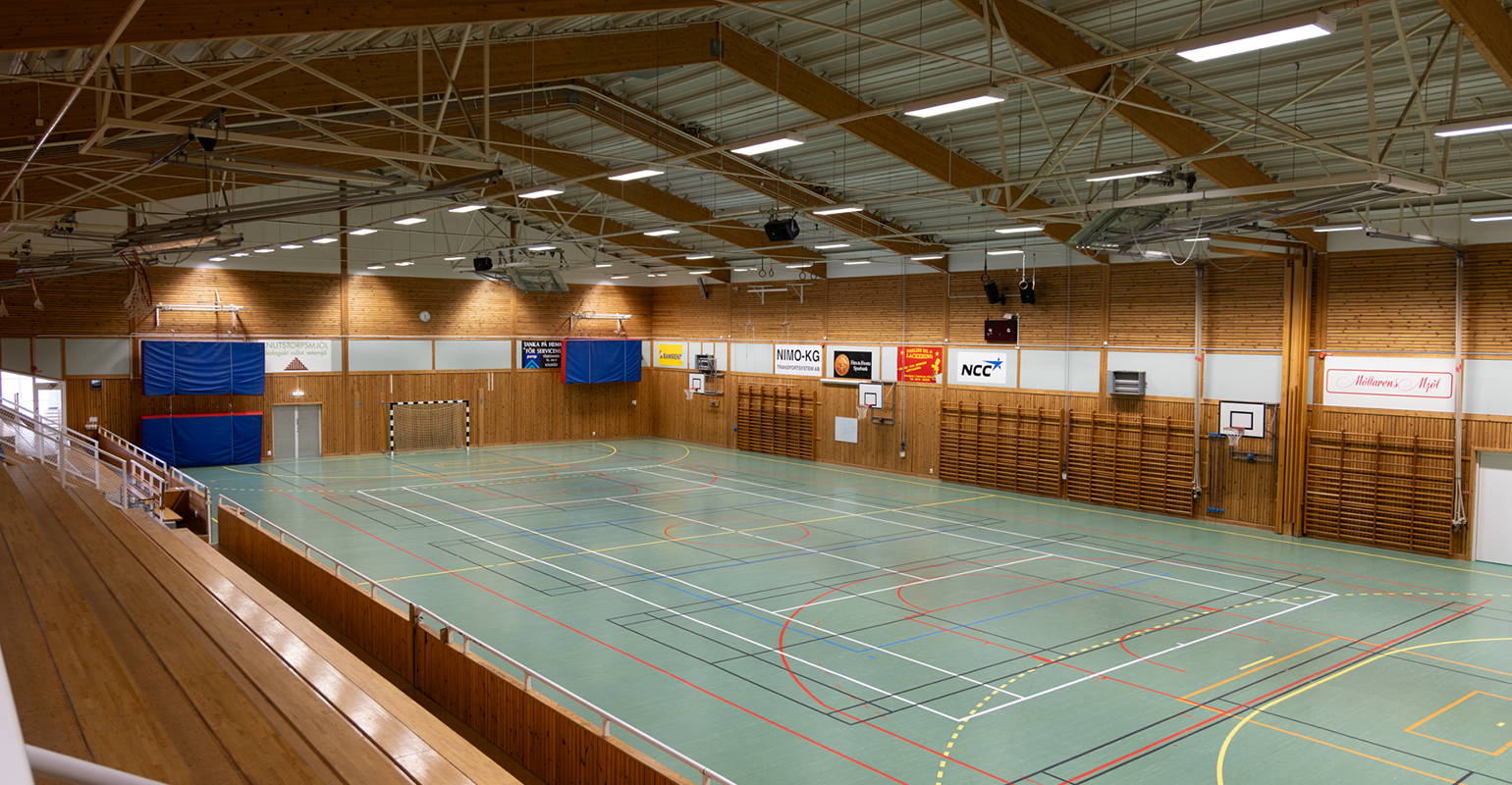Idrottshall med markeringar för flera olika sporter, läktare längs ena långsidan och gott om utrymme för träning, matcher och andra aktiviteter.